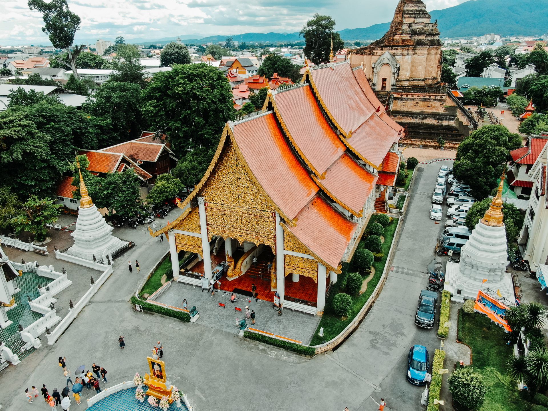 Aerial view of a Chiang Mai temple compound with a gilded hall with orange tiered roofs and a large brick chedi behind it