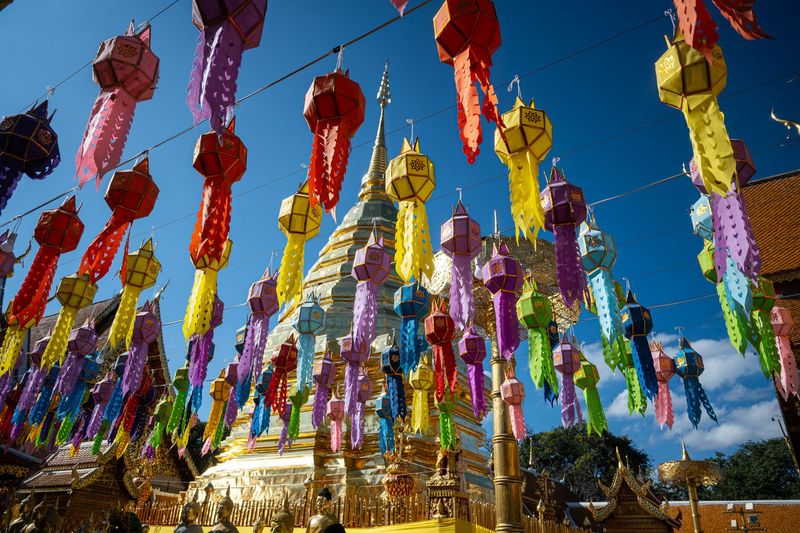 Rows of colourful paper lanterns hang on lines above a golden chedi at a temple in Chiang Mai under a blue sky