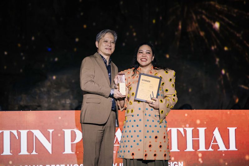 Two people on an awards stage hold a trophy and a “Winner” certificate in front of a lit backdrop.
