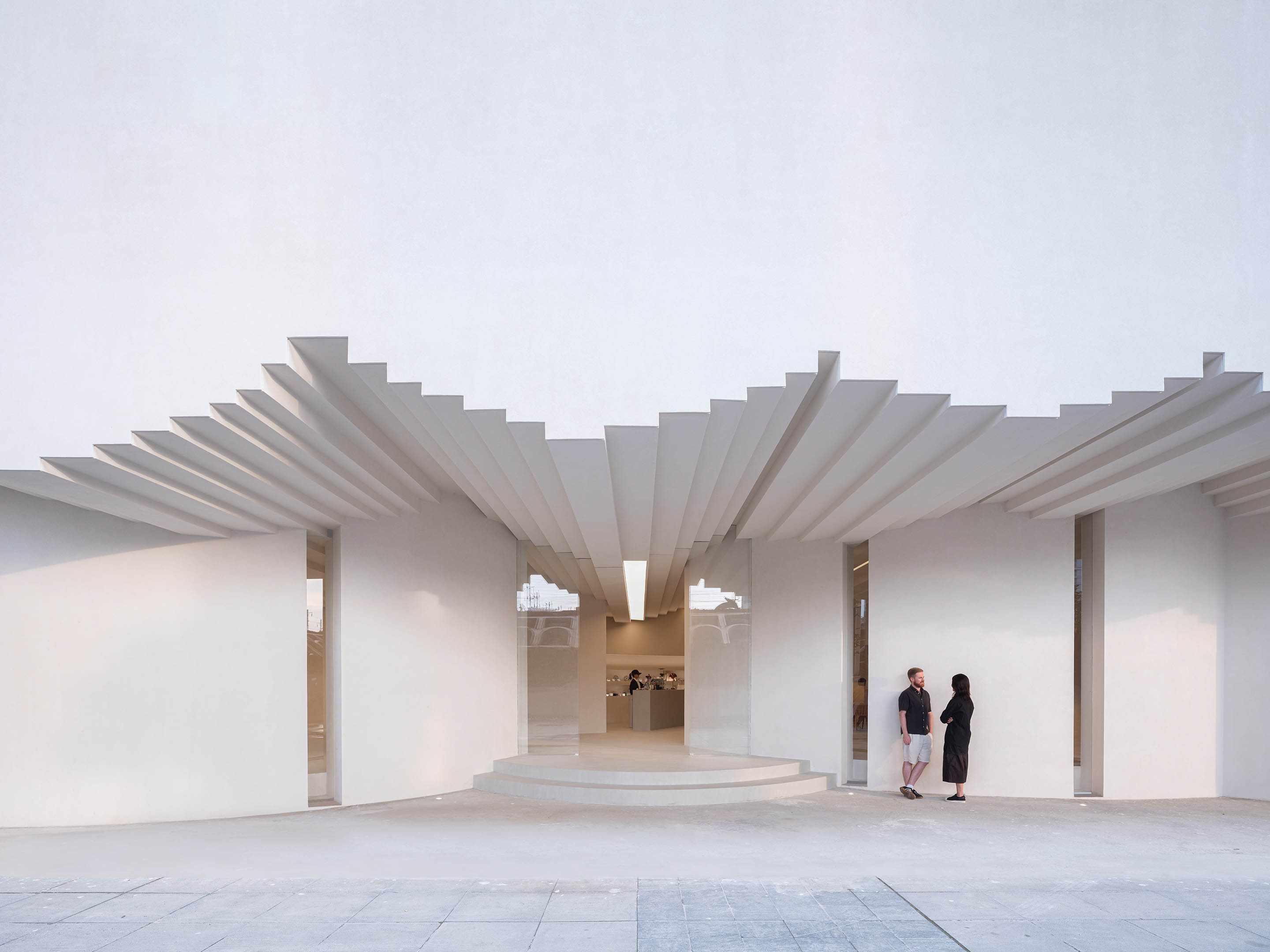 Simple Art Museum: a white pavilion with a stepped, fan-like canopy over a recessed entrance, where two people stand talking.