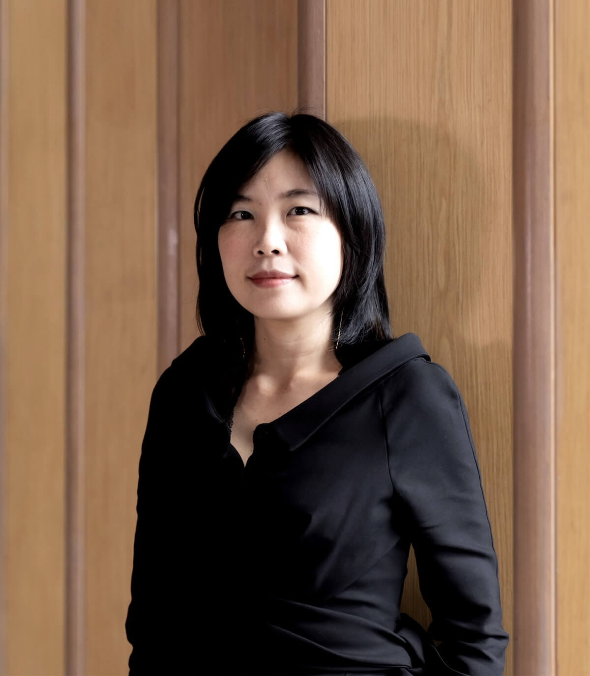 Portrait of Professor Kulthida Songkittipakdee in a black top, standing against wood-panelled walls.
