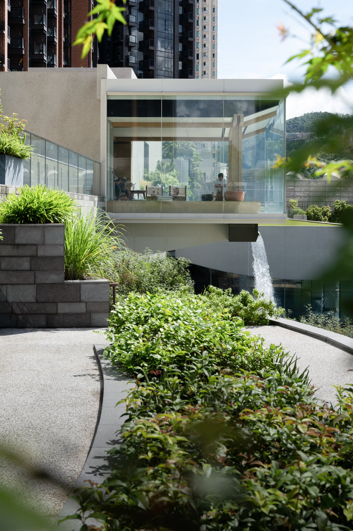 The glass-walled Tea House cantilevering over a planted terrace, with a waterfall dropping beneath it.