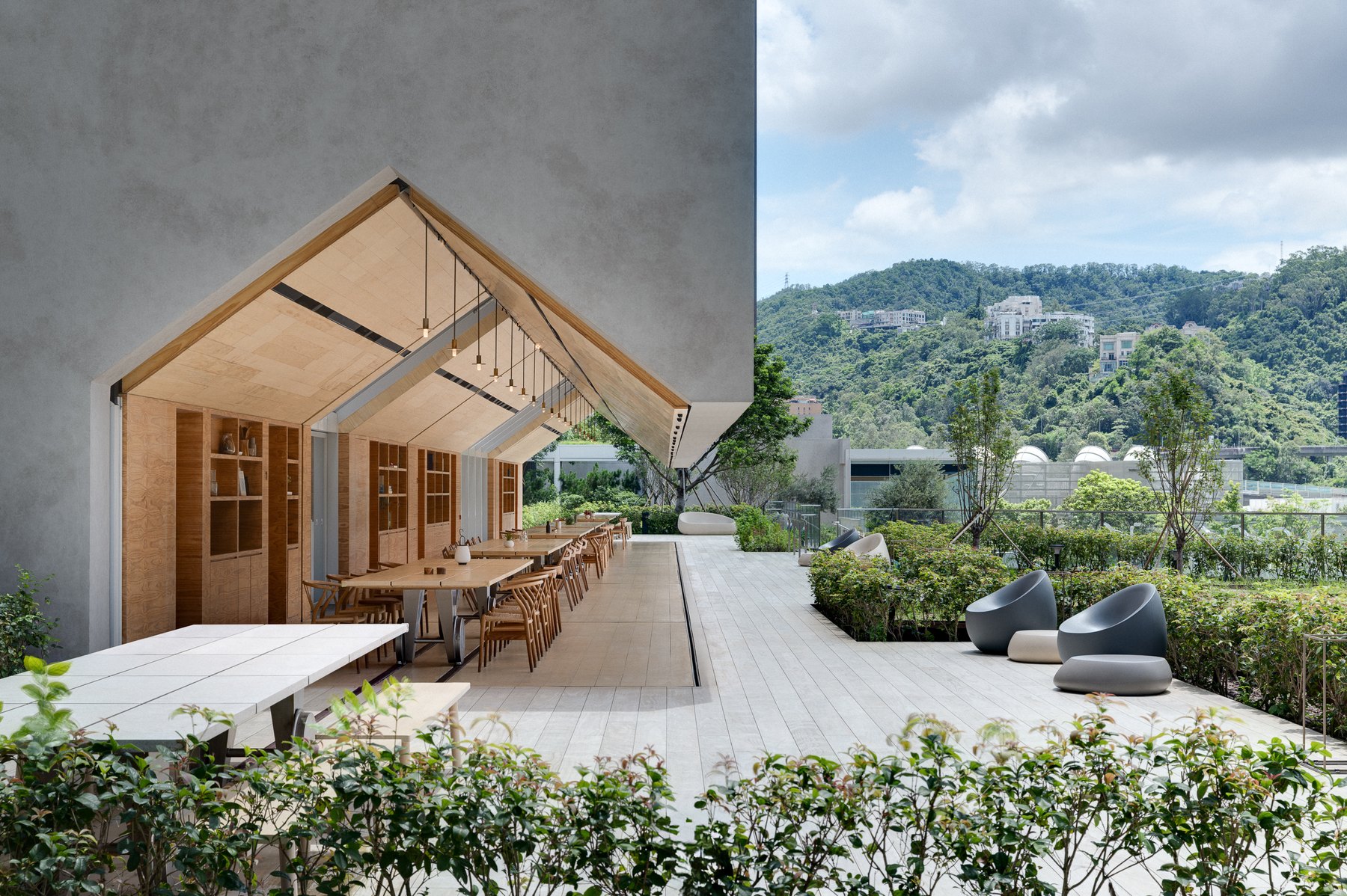 The Farm House terrace with long timber dining tables under a gabled canopy, looking out to planting and wooded hills.